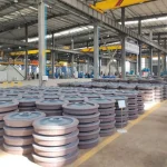 Railway wheels in a manufacturing plant, with wheels in the foreground and production and inspection equipment in the background.