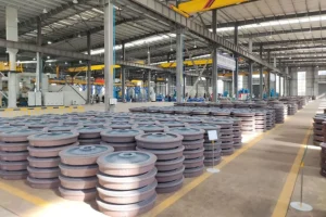 Railway wheels in a manufacturing plant, with wheels in the foreground and production and inspection equipment in the background.